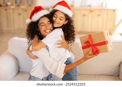 Loving mother embrace daughter, both wearing Santa hats, exchanging gifts on Xmas Day, sitting on sofa in living room - Powered by Shutterstock