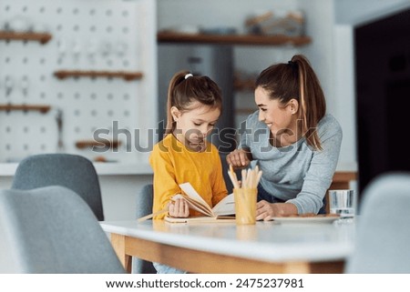 A loving mother encouraging her young daughter and praising her drawing skills as they go through her sketchbook together.