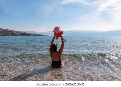 Loving mother swimming with toddler on paradise pebble beach in coastal town Baska, Krk Island, Primorje-Gorski Kotar, Croatia, Europe. Scenic view of coastline of Mediterranean Adriatic Sea in summer - Powered by Shutterstock