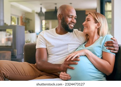 Loving Multi-Racial Couple With Pregnant Woman On Sofa At Home With Multi-Generation Family Behind - Powered by Shutterstock