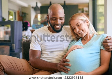 Loving Multi-Racial Couple With Pregnant Woman On Sofa At Home With Multi-Generation Family Behind