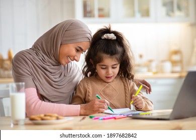 Loving Muslim Mom In Hijab Drawing With Her Little Preschooler Daughter In Kitchen, Happy Islamic Family Sitting At Table And Using Colorful Pencils, Having Fun Together At Home, Free Space