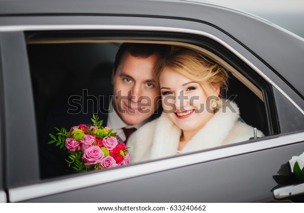 Loving newlywed bride and groom laugh in the retro\
wedding car