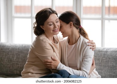 Loving Old Caucasian 60s Mom Sit Relax On Sofa At Home Hug Cuddle Adult Daughter Show Support Comfort. Caring Middle-aged Mother Embrace Grownup Girl Child Caress Feel Supportive. Bonding Concept.