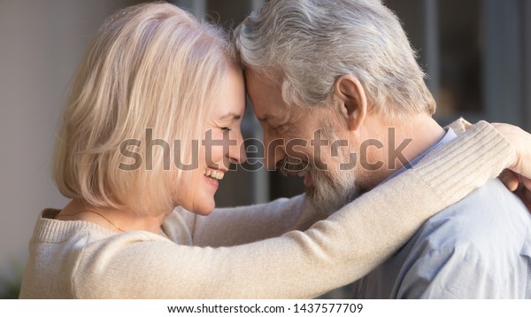 Loving old senior family couple bonding embracing\
touching foreheads, romantic middle aged mature man and woman\
hugging getting closer enjoying moment of affection cuddling, close\
up side view