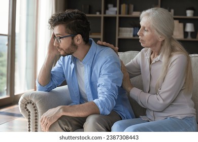 Loving older woman comforting her upset young adult son, gives wise advice in difficult life situation, talking, provide psychological support showing care seated on couch, spend time together at home - Powered by Shutterstock