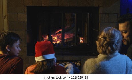 Loving parents with kids sitting at fireplace before New Year enjoying holiday together. - Shutterstock ID 1029529423