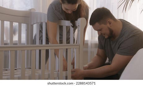 Loving parents together assembling white crib for infant at nursery. Father uses hex key for fixing mounts of baby cradle. Caring wife helps beloved man. Concept of parenthood, childhood and family. - Powered by Shutterstock