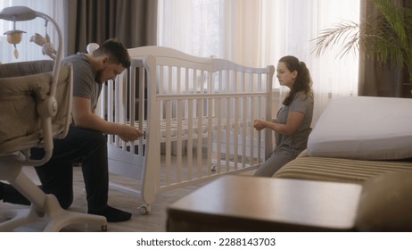 Loving parents together assembling white crib for newborn baby at nursery. Young father uses hex key for fixing mounts. Caring wife helps beloved man. Concept of parenthood, childhood and family. - Powered by Shutterstock