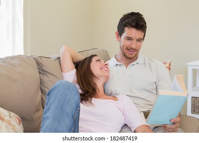 Loving Relaxed Young Couple Reading Book On Couch At Home