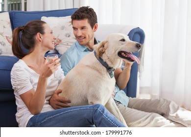 Loving Relaxed Young Couple With Wine Glass And Pet Dog Sitting In Living Room At Home