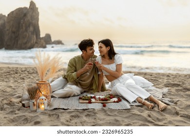 Loving romantic couple having picnic on sandy beach near ocean, drinking wine and enjoying date in the evening together at coastline, copy space - Powered by Shutterstock