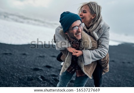 A loving romantic couple of tourists have fun while walking along the beach with black volcanic sand and admire the great ocean waves. Travel, leisure, tourism.