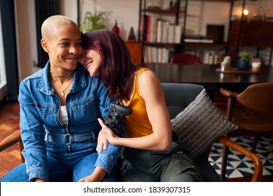 Loving Same Sex Female Couple Sitting On Sofa At Home Gaming Together