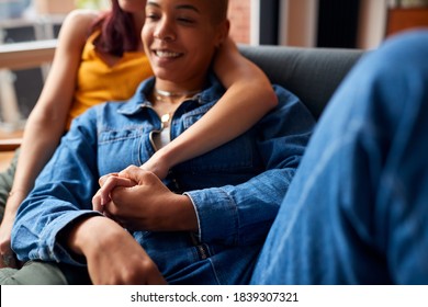 Loving Same Sex Female Couple Holding Hands Lying On Sofa At Home Watching TV And Relaxing Together