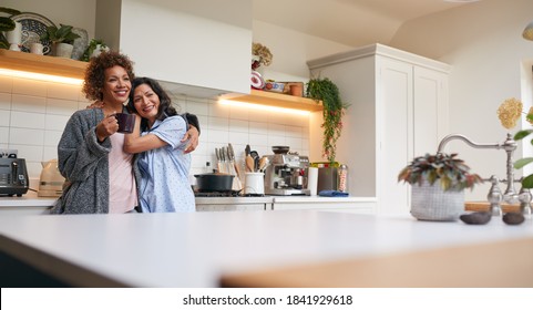 Loving Same Sex Mature Female Couple Wearing Pyjamas Hugging In Kitchen At Home Together