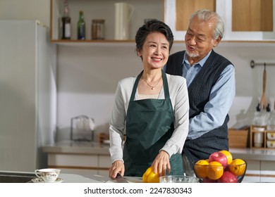 loving senior asian man husband helping wife tying up apron in kitchen at home - Powered by Shutterstock