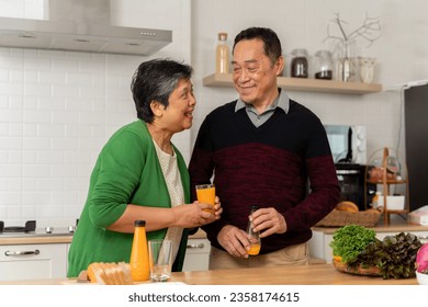 Loving senior couple in aprons toasting each other with orange juice and preparing healthy dinner while spending time at home. Different fruits on table. Healthy food at home. - Powered by Shutterstock