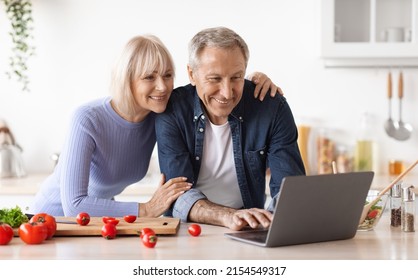 Loving Senior Couple Cooking Together At Home, Cheerful Elderly Man And Woman Looking For Recipes On Internet, Using Modern Laptop, Making Healthy Dinner, Kitchen Interior, Copy Space