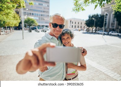 Loving senior couple embracing and taking a selfie on mobile phone outdoors. Tourist taking self portrait during a foreign city vacation. - Powered by Shutterstock