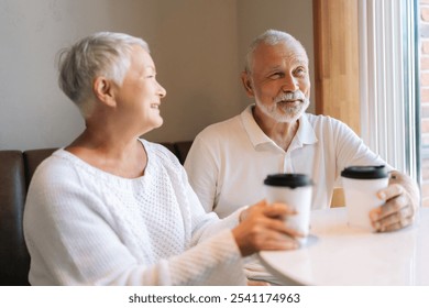 Loving senior couple enjoying cozy cafe date, smiling and chatting over coffee sitting hugging by window, showcasing enduring love and happiness. Concept of active aging and happy golden years. - Powered by Shutterstock