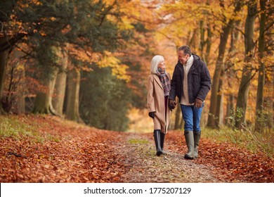 Loving Senior Couple Holding Hands As They Walk Along Autumn Woodland Path Through Trees Together - Powered by Shutterstock