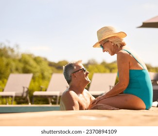 Loving Senior Couple On Holiday Wearing Swimming Costumes Relaxing By Hotel Swimming Pool - Powered by Shutterstock