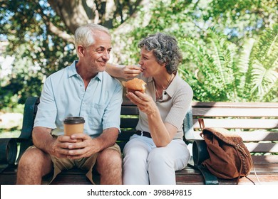 Loving senior couple sitting on a park bench having coffee and muffins. Tourist relaxing outdoors on a park bench. - Powered by Shutterstock