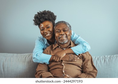 Loving senior man embracing his daughter while sitting on sofa smiling. An attractive young woman embracing her grandfather from back. Senior African American man and granddaughter smiling  - Powered by Shutterstock