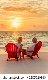 Loving Seniors Wearing White Casual Clothing Relaxing On Red Chairs Watching Sunrise Over Ocean On Tropical Beach Bahamas 