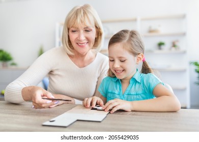 Loving smiling mature woman sitting at table with little girl engaged in game assemble jigsaw together, happy grandmother playing having fun with preschooler kid making picture connect puzzle pieces - Powered by Shutterstock