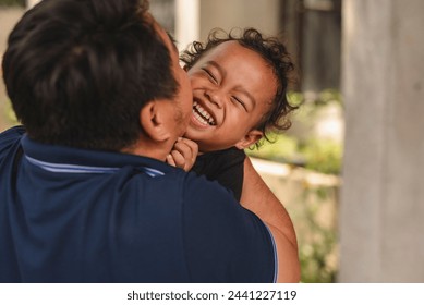 A loving Southeast Asian man engages in playful bonding with his young son outside their house, showcasing a joyful family moment. - Powered by Shutterstock