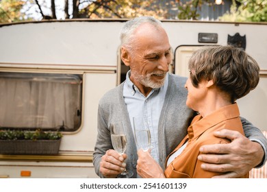 Loving tender old senior couple hugging celebrating with wine toasting anniversary while traveling by trailer motor home camper van. Active seniors concept - Powered by Shutterstock