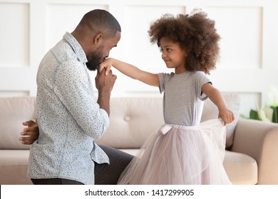 Loving Young African American Dad Standing On Knee Thanking Cute Little Child Daughter For Dance, Happy Black Father Play With Small Kid Girl Princess Holding Kissing Hand Having Fun At Home Together