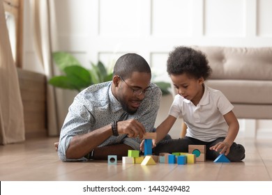 Loving young african American dad lying on floor with little son playing with building bricks, caring black father spend enjoy time with toddler kid learning using toy blocks engaged in funny activity