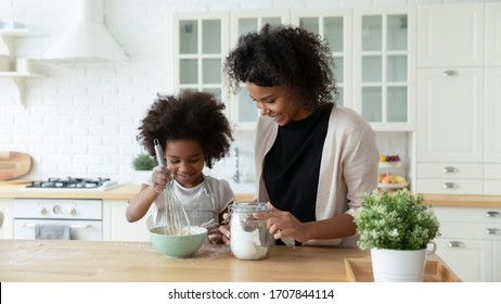 Loving Young African American Mother Teach Small Biracial Daughter Bake In Kitchen, Happy Caring Ethnic Mom And Little Girl Child Preparing Pancakes Or Biscuits, Make Breakfast At Home Together