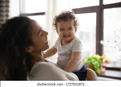 Loving young african American mother hold in arms cute funny infant toddler showing first teeth, caring happy biracial mom hug embrace smiling little baby girl child, motherhood, childcare concept - Powered by Shutterstock