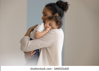 Loving Young Biracial Mother Hold In Hands Embrace Small Newborn Baby Child. Caring African American Mom Lean To Chest Hug Cuddle Little Infant Child, Enjoy Tender Close Family Moment Together.