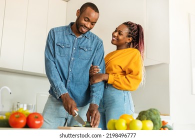 Loving Young Black Man Cooking Delicious Dinner For His Beautiful Wife, Cutting Vegetables, Light Kitchen Interior, Copy Space. Love, Affectionate, Family Lifestyle Concept