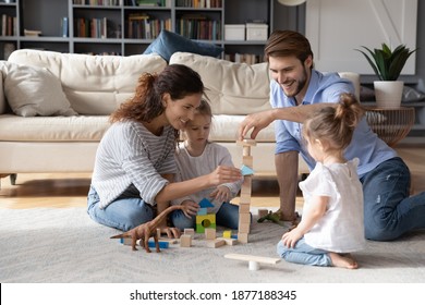 Loving young Caucasian family with two small daughters sit on floor in living room play with building bricks. Caring parents feel playful construct with colorful blocks with little girls children.