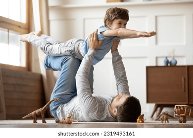 Loving young Caucasian father lying on floor at home have fun play with cute excited little son. Caring dad imitate plane fly, engaged in funny game together with happy small preschooler boy child. - Shutterstock ID 2319493161