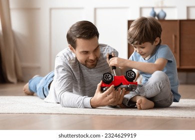 Loving young Caucasian father sit on floor feel playful repair fix toy car together with little 8s son. Caring happy dad play with automobiles with small preschooler boy child at home on weekend. - Powered by Shutterstock