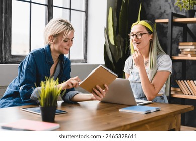 Loving young caucasian female lgbtq couple lesbians reading books, studying together at home office, doing homework, doing paperwork, preparing for college university - Powered by Shutterstock