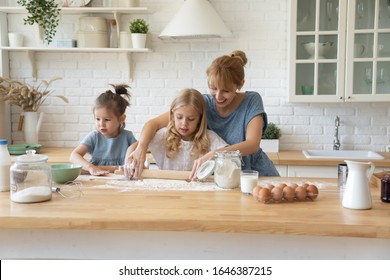 Loving Young Caucasian Mother Cooking Baking Together With Small Preschooler Daughters In Modern Kitchen, Caring Millennial Mom And Little Girls Children Roll Dough Do Bakery Pastries Cookies At Home