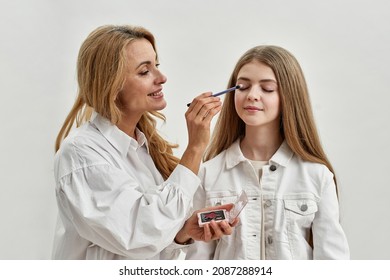 Loving young Caucasian mother do makeup for happy teenage daughter. Caring middle-aged mom have fun with teen girl child, have beauty routine together. Isolated on white studio background.