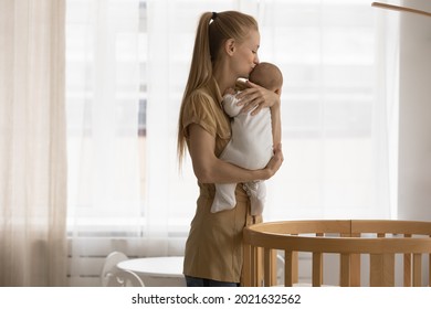 Loving young Caucasian mother lull put to bed cradle small baby infant kid child in cozy children bedroom. Caring mom hug caress little newborn son or daughter to bassinet. Motherhood concept.