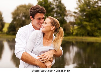 Loving Young Couple Embracing By The Lake In Summer Morning