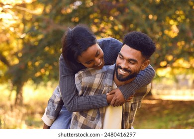 Loving Young Couple With Man Giving Woman Piggyback Against Background Of Autumn Leaves - Powered by Shutterstock