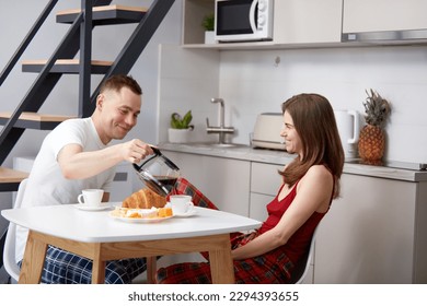 Loving young couple, man and woman having morning breakfast at home in kitchen. Husband pouring coffee to his smiling wife. Concept of love, relationship, family, emotions, lifestyle, support and care - Powered by Shutterstock