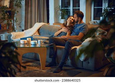 Loving young couple, man and woman sitting on sofa in evening at home,, hugging, cuddling and watching tv together. Concept of family, leisure time, relaxation, childhood and parenthood - Powered by Shutterstock